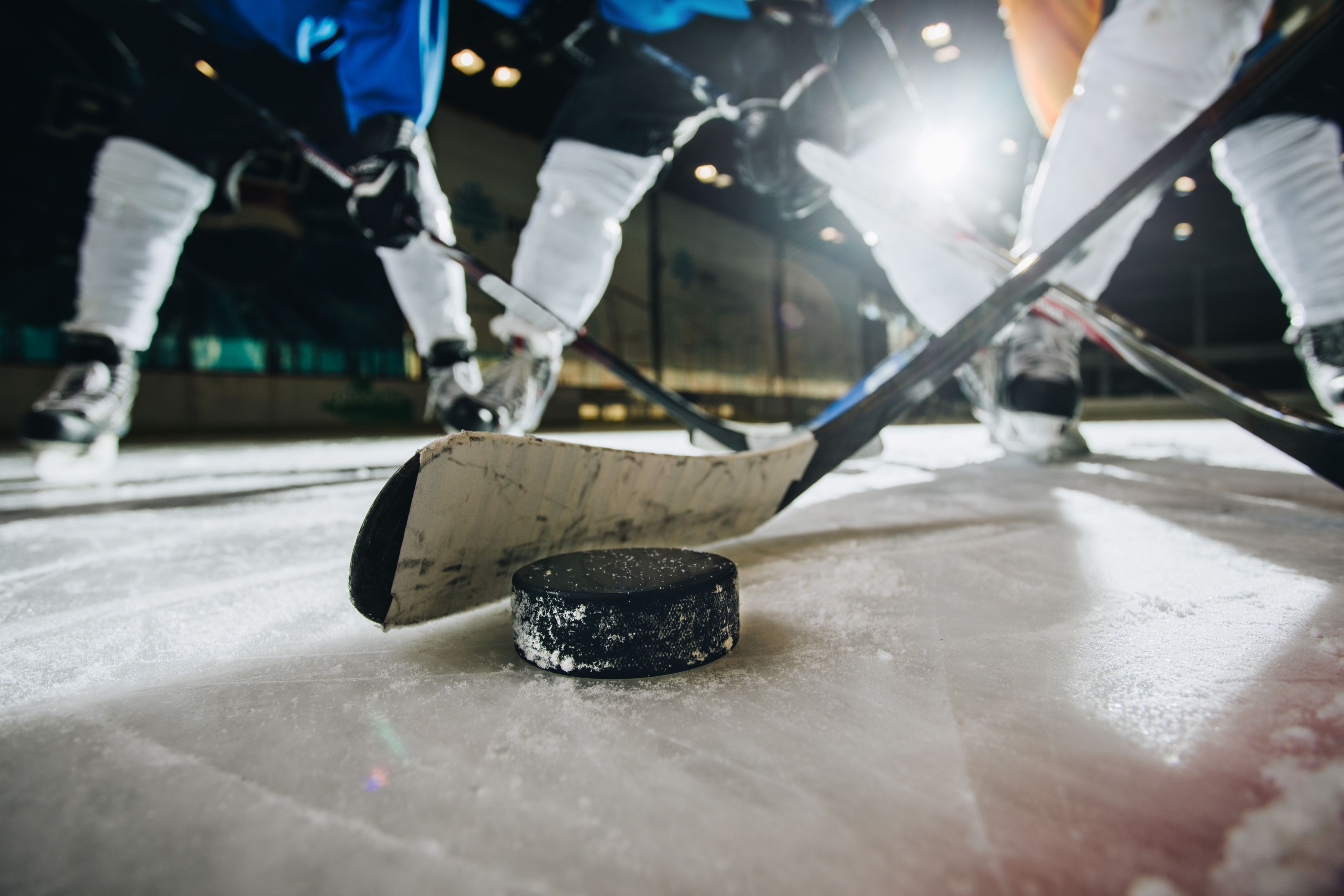 Close up of hockey puck and stick during a match with players in the background.